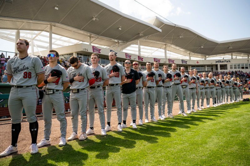 Northeastern men's baseball players lined up with hands over their hearts for the national anthenm.