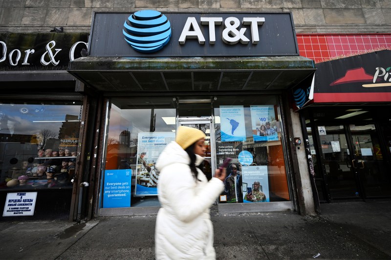 Person wearing white jacket and yellow beanie walking in front of AT&T store.
