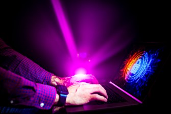 A person using a laptop in front of a purple beam of light.