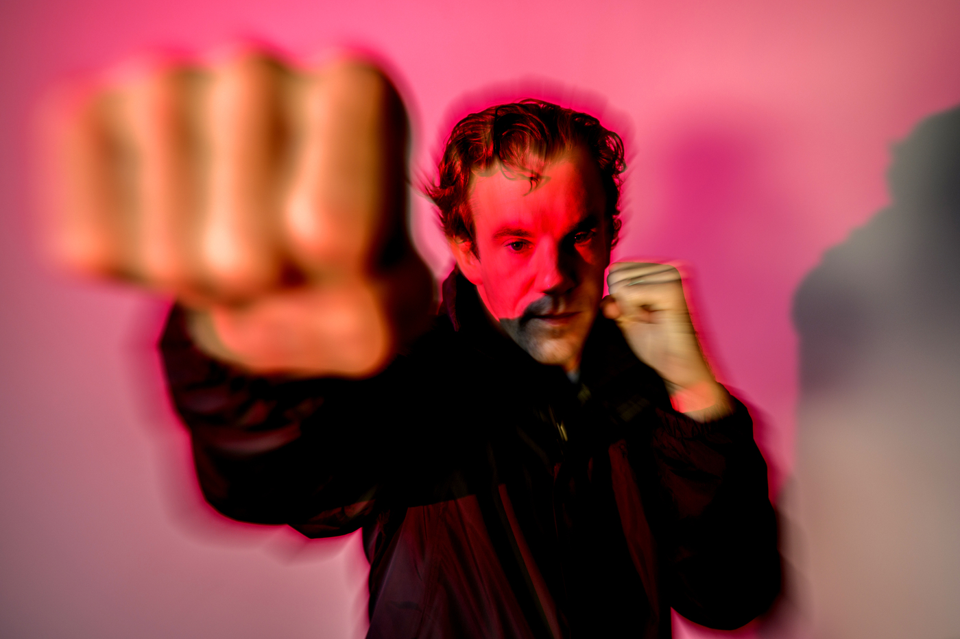 A person throwing a punch in front of a pink background, captured in a blurry image.