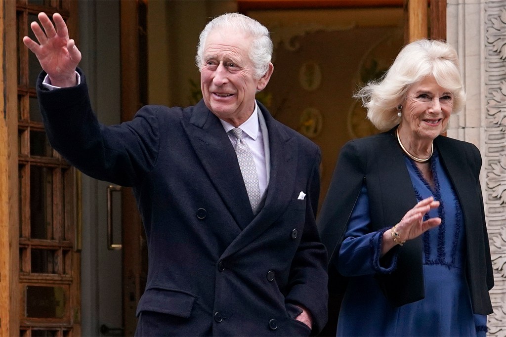 King Charles III waving as he exists a building next to Queen Camilla.