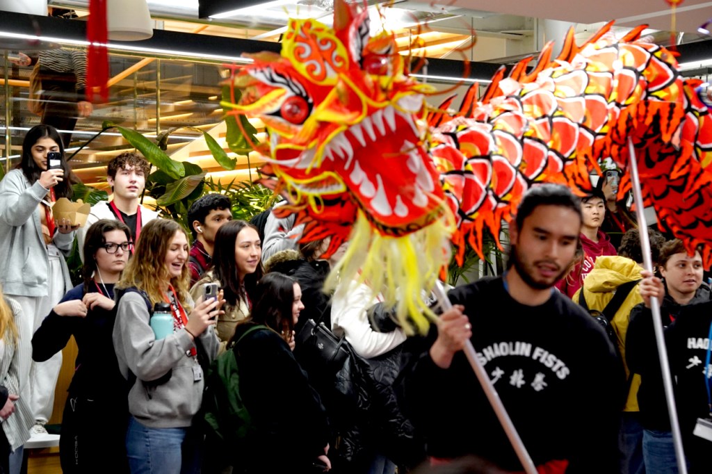 Audience members cheer to performers holding up a large dragon puppet made of paper.