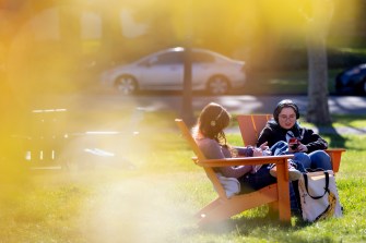 Two people sit outside in orange-colored chairs while they soak up the sun.