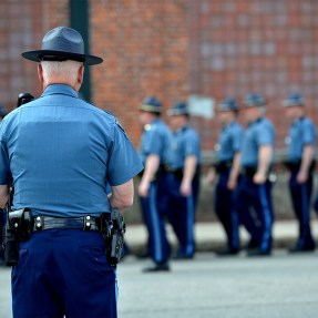 A MA state trooper seen from behind watching other state troopers stand in a line.