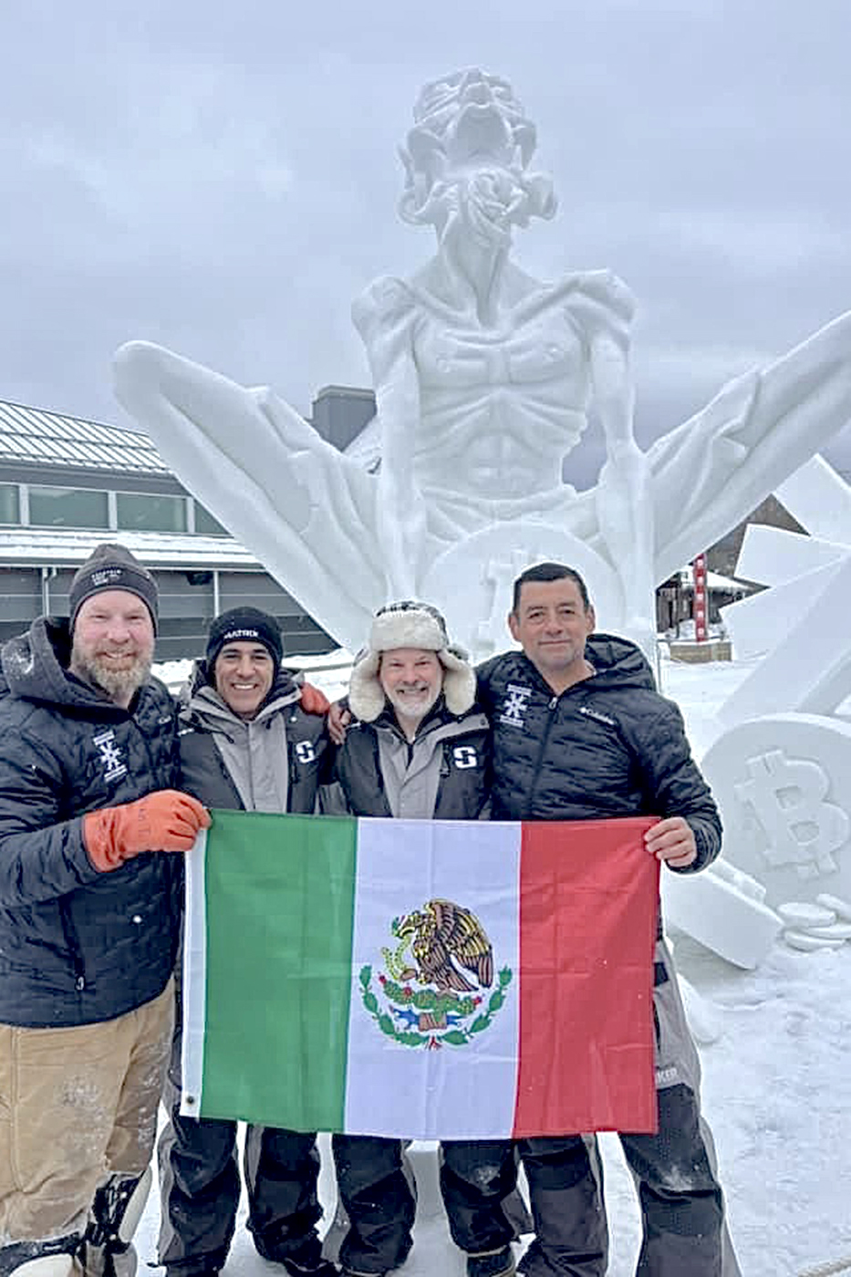 Four people pose in front of a winning snow sculpture at the 2024 Breckenridge International Snow Sculpture Championships.