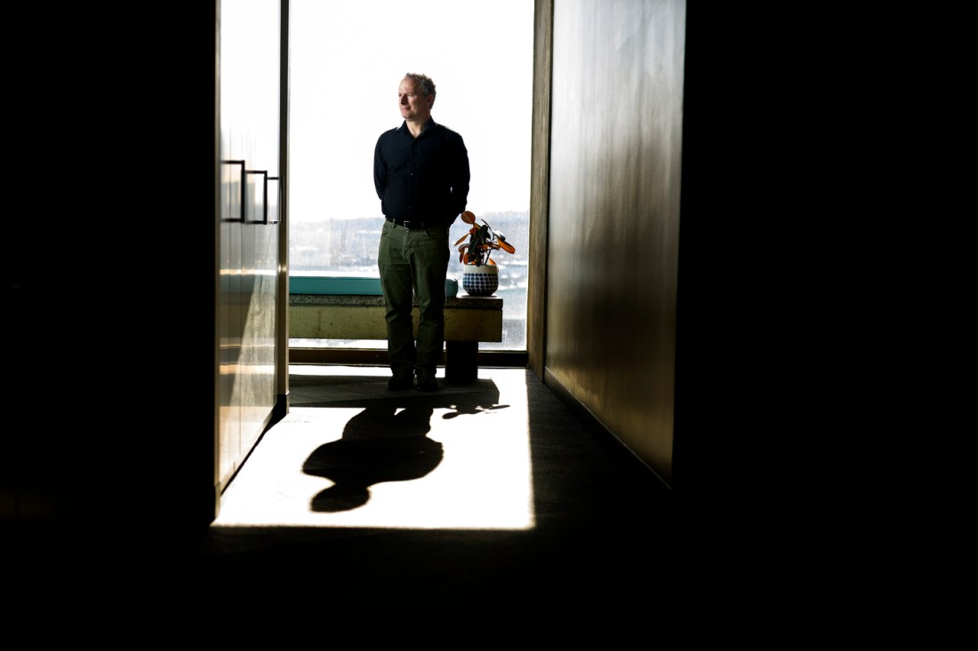 David Lazer standing at the end of a hallway in front of a large window.