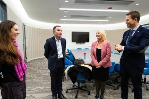 Four people stand in a brightly lit room talking.