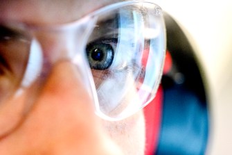 A close-up image of a person with blue-colored eyes wearing laboratory goggles.
