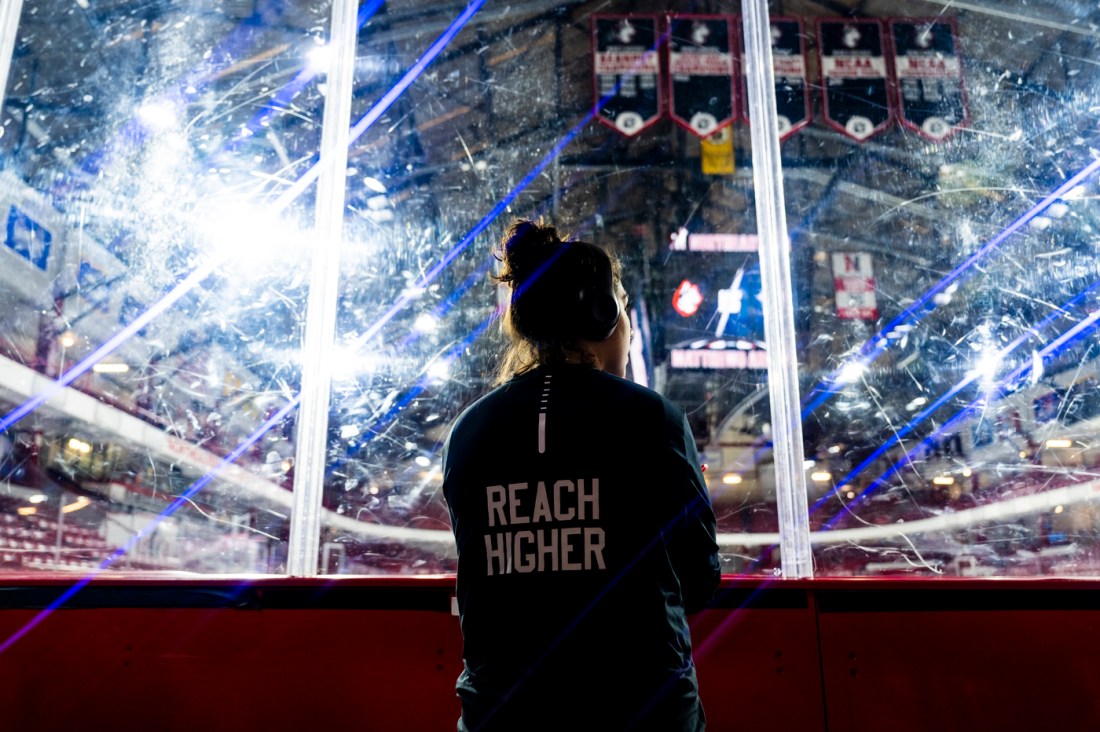 A person wearing a jacket that says 'REACH HIGHER' on the back of it wearing headphones and looking out on the ice at Matthews Arena.