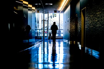 A person casts a silhouette while walking down a hallway toward a large set of windows.