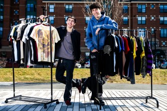 Joaquin Crosby-Lizarde and Josh Maizes posing for portraits with racks of clothing for sale.