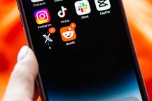 A phone displaying several social media apps including Instagram, TikTok, X, and Reddit.