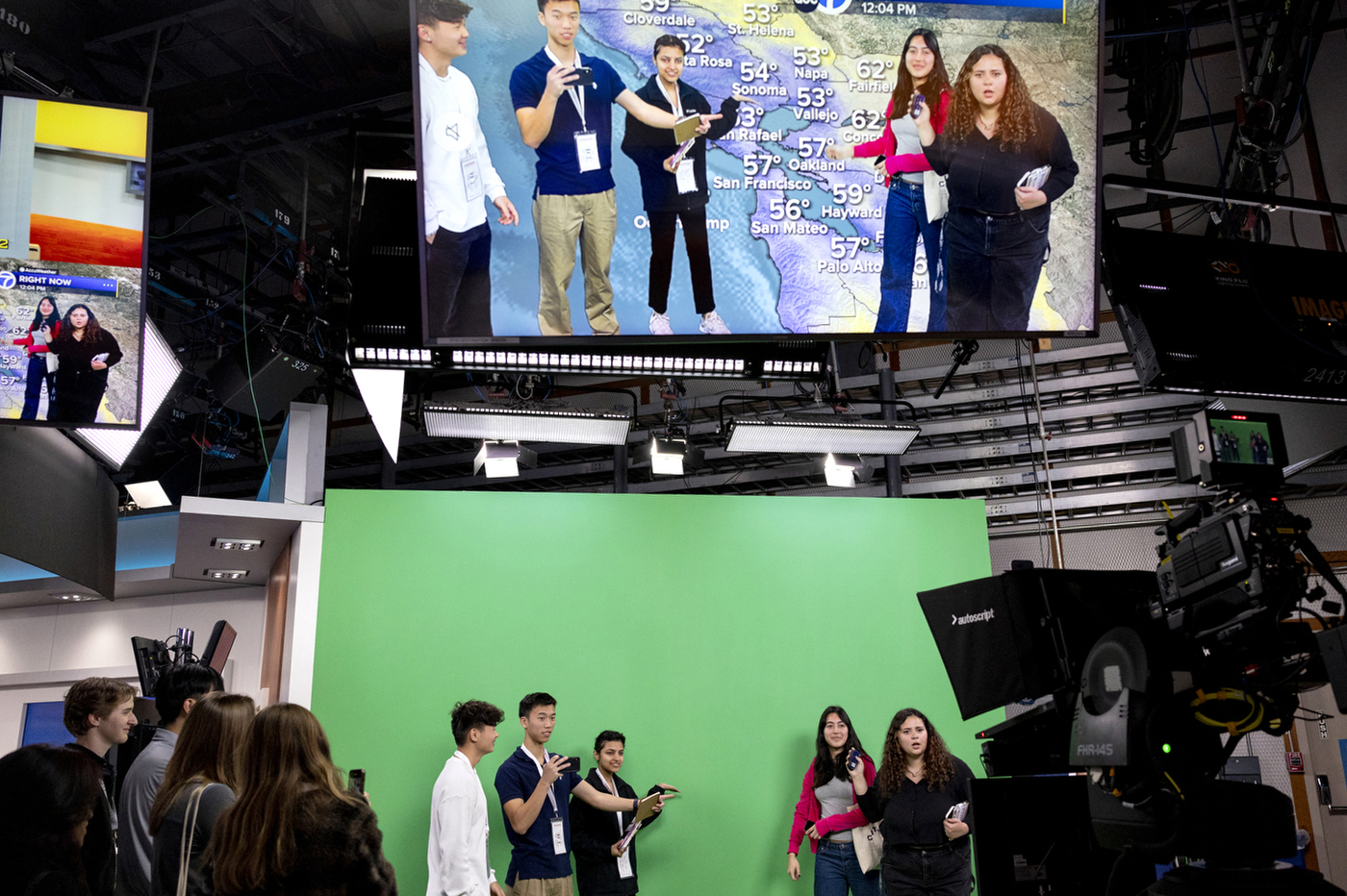 Multiple people stand in front of a green screen inside a news station studio.