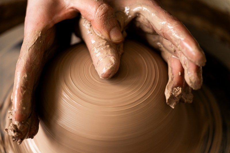David Chatson throwing pottery on a wheel. This closeup shows their fingers shaping a spinning piece of clay.