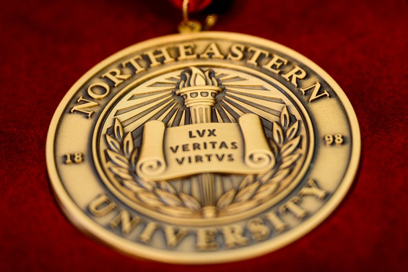 The front of a gold medal showing the Northeastern logo. 