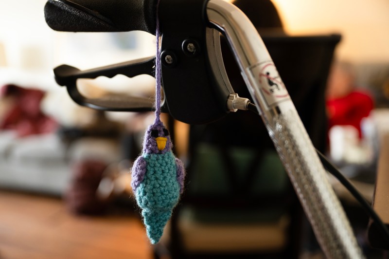 A purple and blue crocheted bird hanging from a walker.