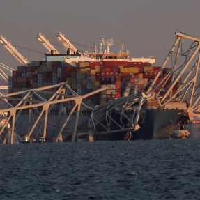 A cropped image showing a cargo ship with the bridge collapsed around it.