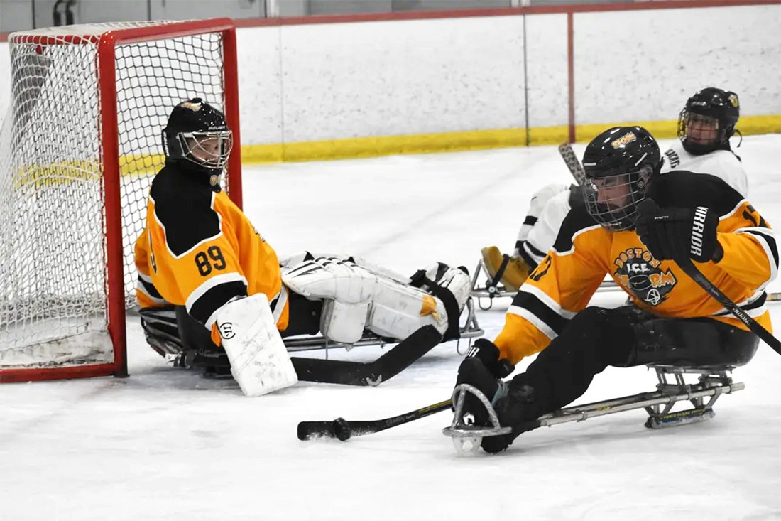 Hockey players on sleds sliding on the ice, shifting the puck away from their goal.