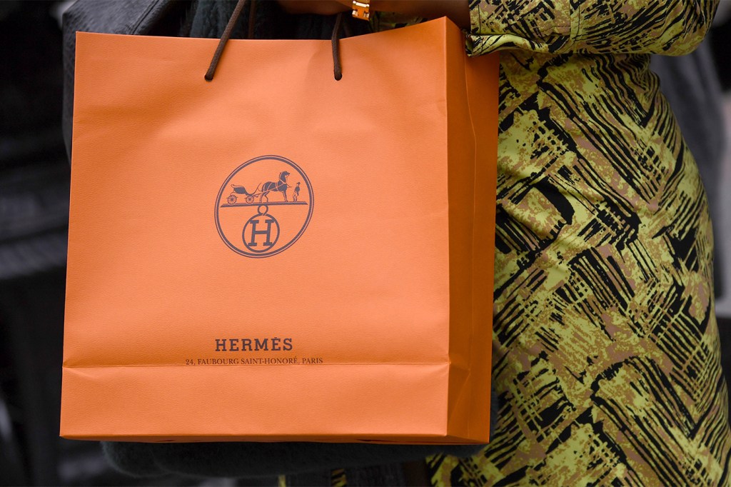 A person holding an orange retail Hermes bag.