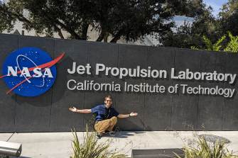 Ethan Holand in front of a sign outside of the NASA Jet Propulsion Laboratory.