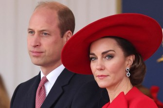 Prince William wearing a suit and Princess Kate wearing a red dress and red hat.