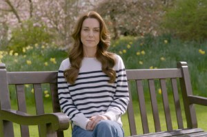 Screen capture of Kate Middleton's announcement with her sitting on a bench in a garden wearing jeans and a striped shirt.