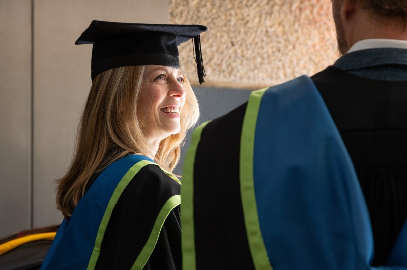 Woman wearing cap and gown smiling.