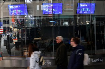 People walking by televisions showing market trading information.