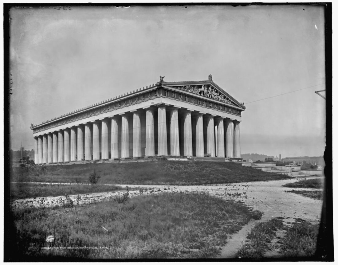 A black-and-white photo of a Greek-style temple with columns and a pointed roof on a wide plain. 