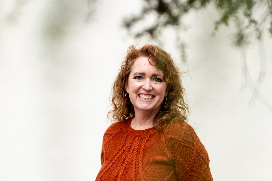 Portrait of Jaci M. Urbani, smiling outside and wearing an orange sweater.
