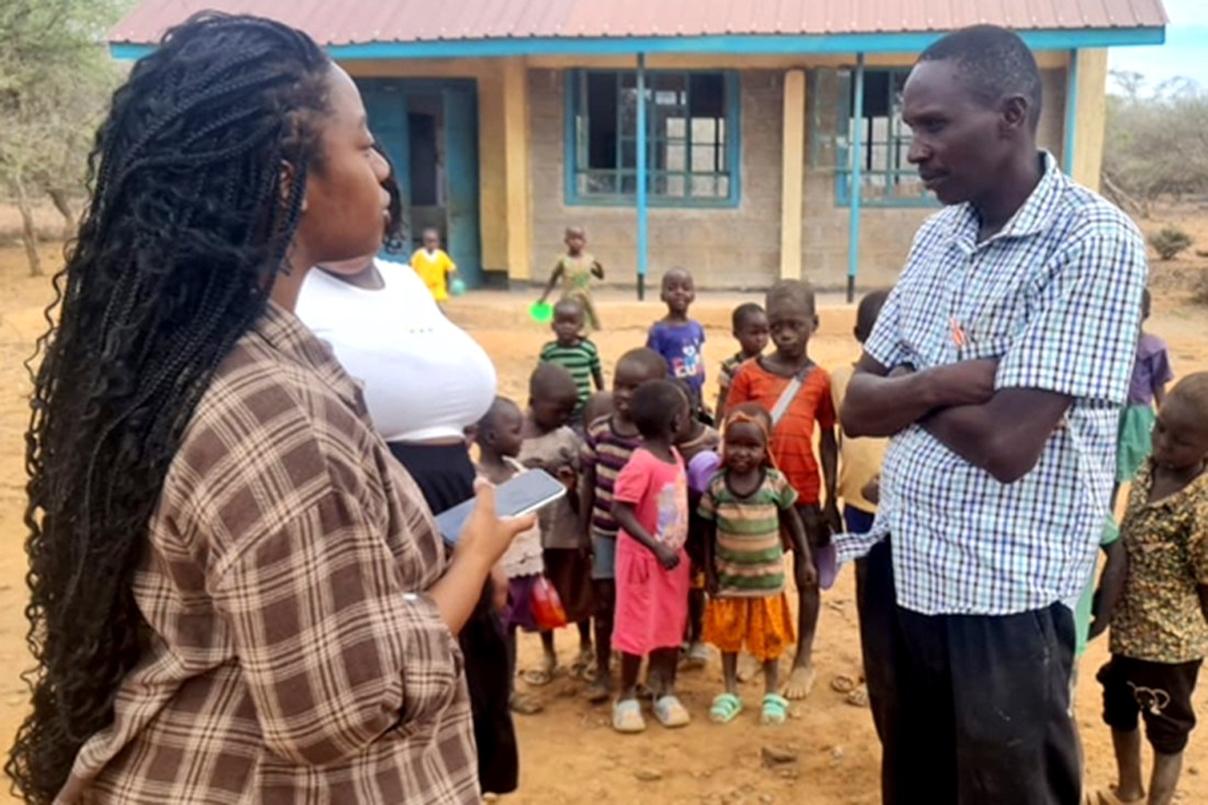 Leah Oruko speaking with a man in front of a group of children in Kenya.