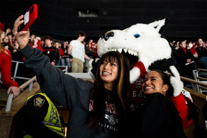 Two students in stands take a selfie with Paws in the background.