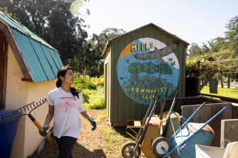 A person walks past a shed with a brightly colored mural with yellow text: "Mills Community Farm."