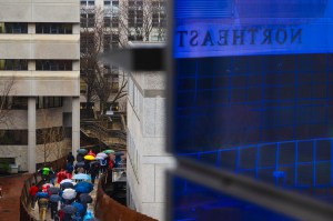 A sea of people with multi-colored umbrellas walking across a bridge on a rainy day.