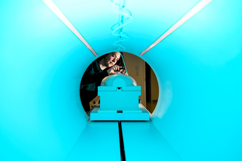 A photo shot through an MRI machine of Northeastern graduate and cognitive research scientist Olivia Rowe working on the equipment.