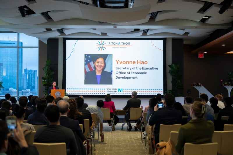 Yvonne Hao speaking at a podium in front of a microphone before a screen that displays a picture of her, her name, and her title.