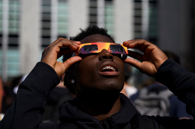 A student wearing eclipse viewing glasses looking up at the sun.