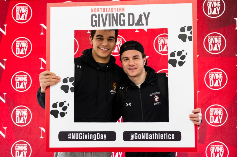 Two people posing with a Giving Day photo prop.