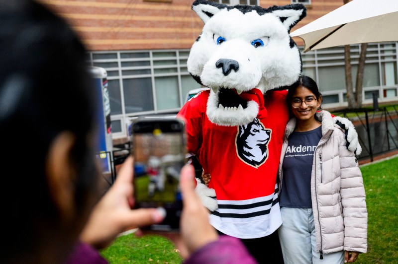 The Northeastern husky mascot Paws poses with a student for a photo.