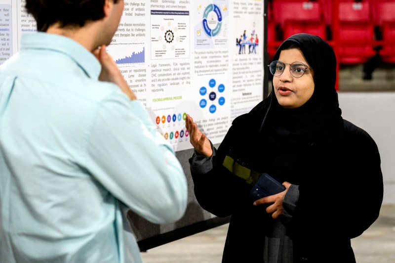 A student gesturing while explaining their project poster at the RISE Expo. 