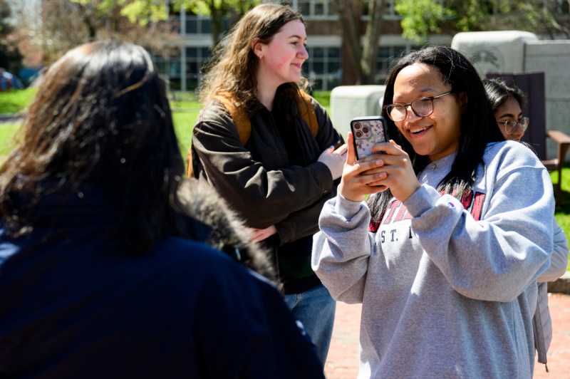 A person wearing a grey-colored sweatshirt takes a picture of another person outside during final exam week.