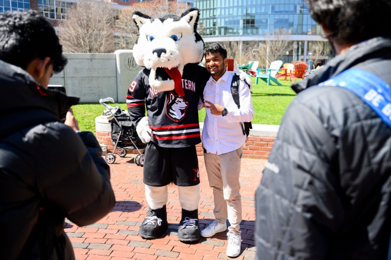 A person poses with a husky mascot outside on a sunny day.
