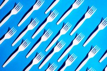 Plastic forks lined up on an angle on a blue background.