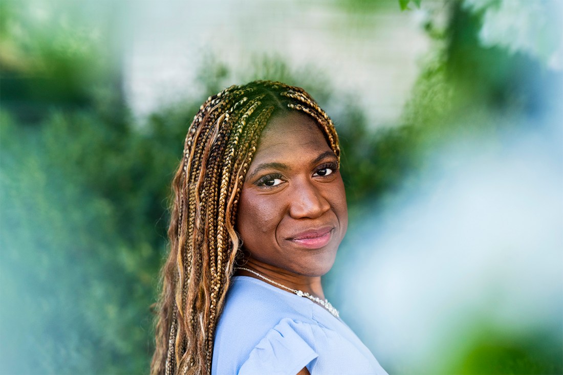 Headshot of Rebecca Bamidele. She's outside amongst greenery, wearing a periwinkle dress and with hair in braids.