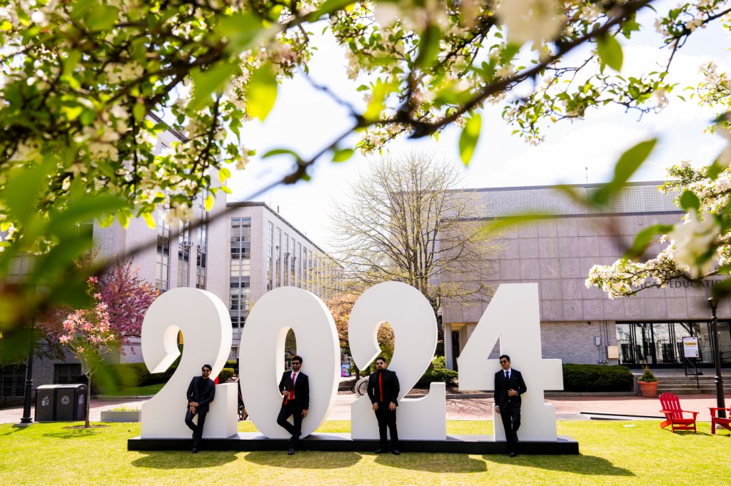 Four people pose outside for a picture in front of a massive, white 2024 sign.