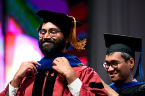 A person wearing regalia has a hood placed over them during a ceremony at Northeastern's Matthews Arena.