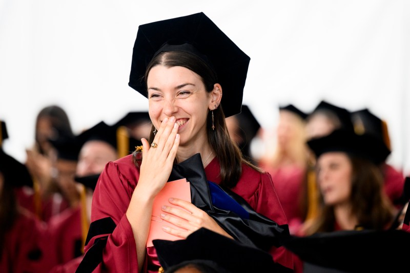 A student laughing and covering their mouth at the Doctor of Philosophy Hooding.