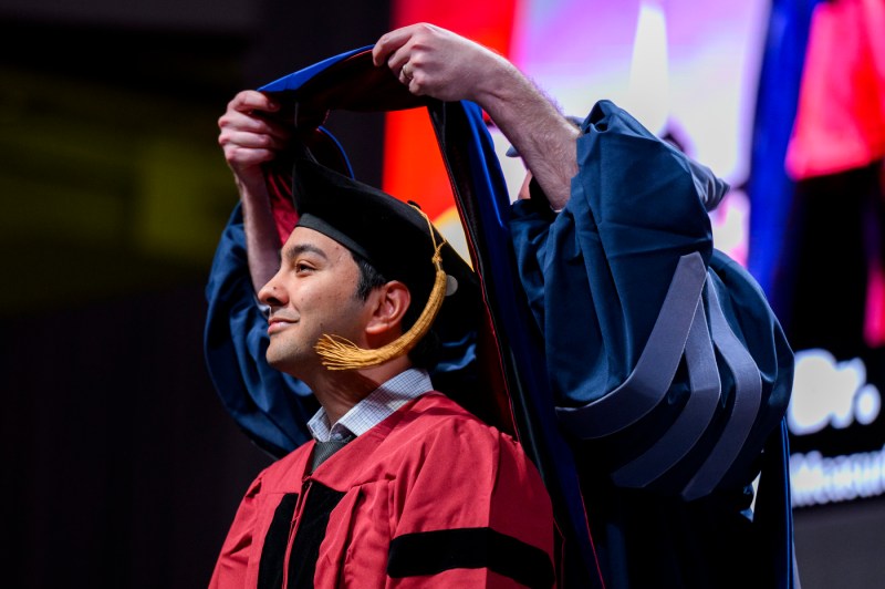 A student getting their hood placed around them at the Doctor of Philosophy hooding.
