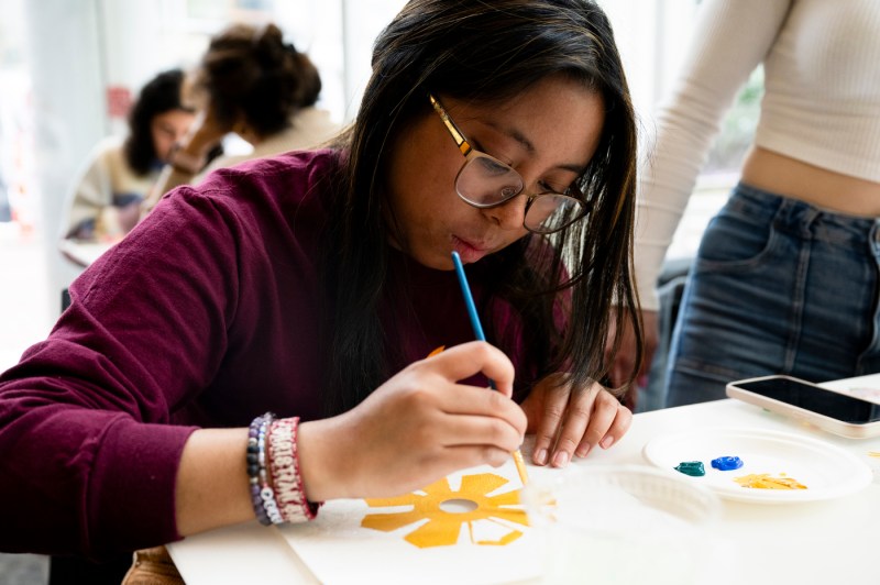 Student painting a yellow flower on their graduation cap. 