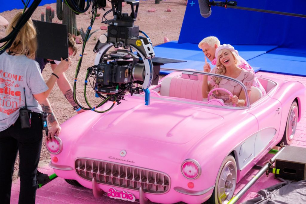 A behind the scenes shot of Margot Robbie and Ryan Gosling in a pink car filming on the set of Barbie.